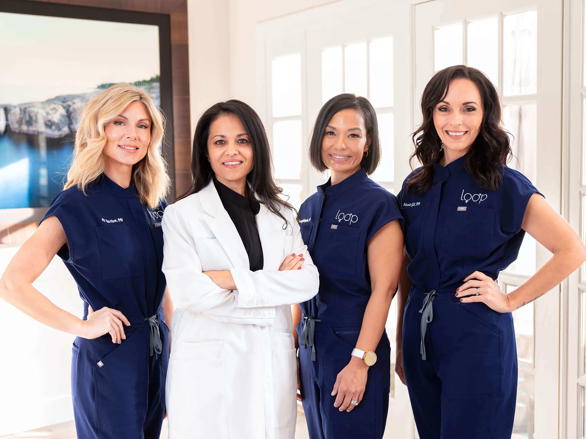 Four Loop Wellness Clinic team members, one in a white lab coat and three in navy scrubs, smiling inside the clinic